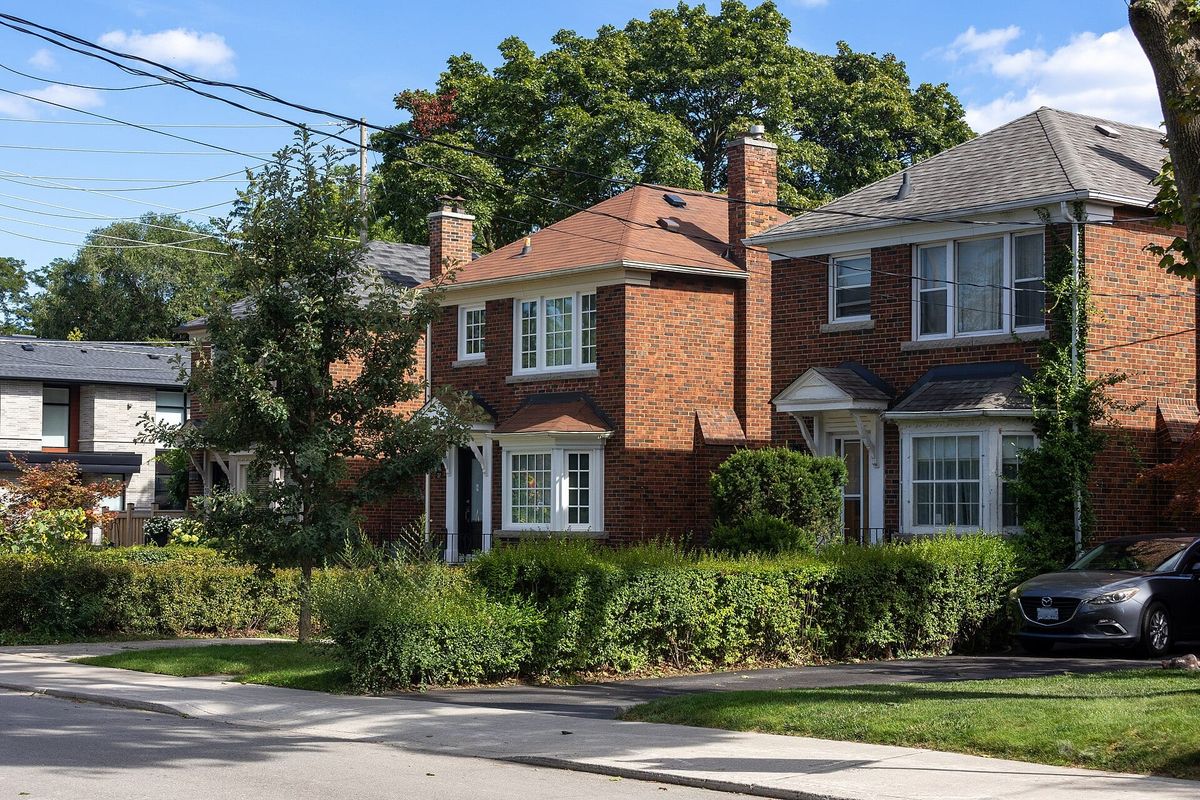 Brick houses behind green lawns and hedges along Rumsey Road in Leaside, Toronto.