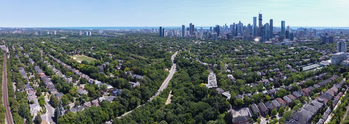 An aerial view south over the tree-covered ravines and houses of Rosedale, Toronto, with the downtown skyline behind.